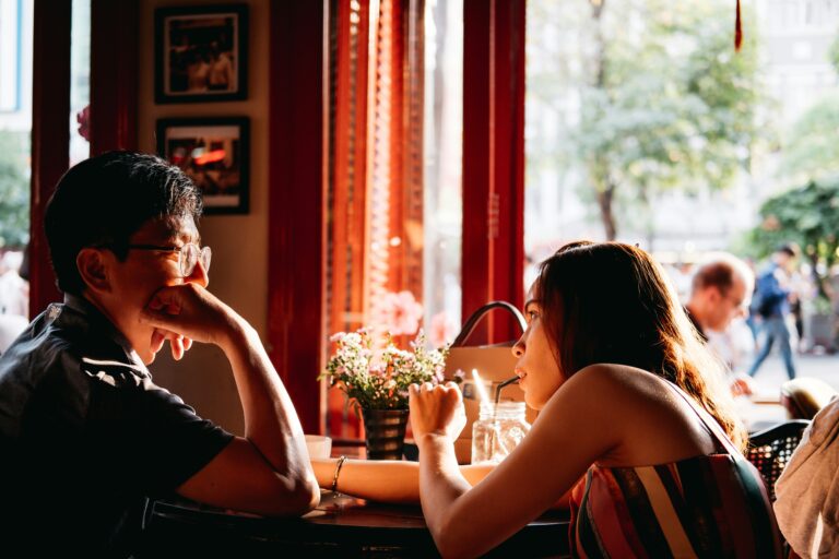 Couple having an engaging, authentic conversation at a coffee shop, showing how real connection happens through being genuinely interesting rather than using pickup lines